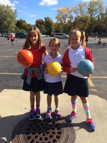 three girls hold volleyballs at recess