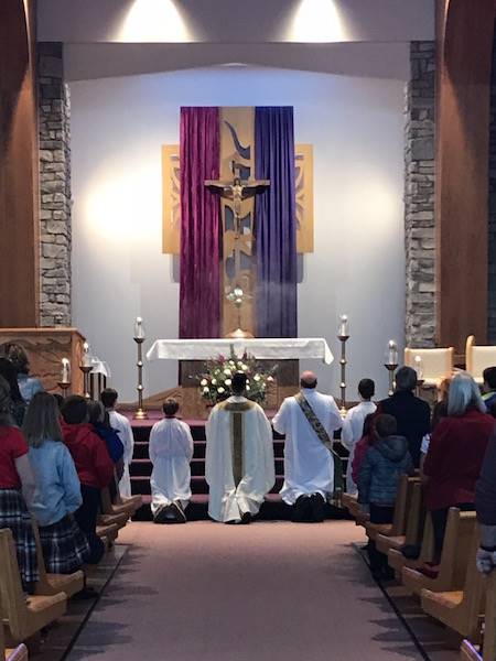 church altar with advent pink and purple with celebrants and server kneeling in eucharistic adoratio