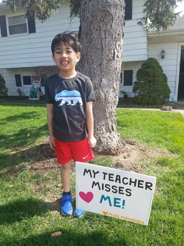 boy standing by sign reading my teacher misses me sign 