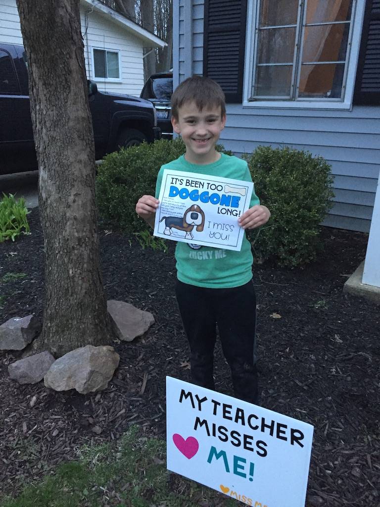 boy standing by sign reading my teacher misses me sign 