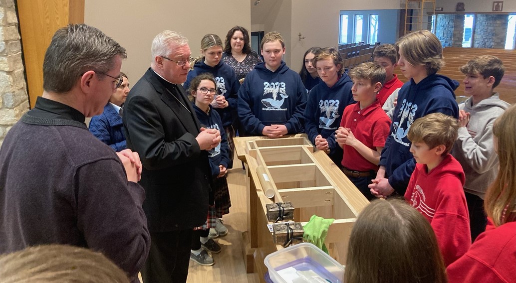 bishop Woost and Fr. Tom place the Relics in the new altar with the 7th and 8th graders