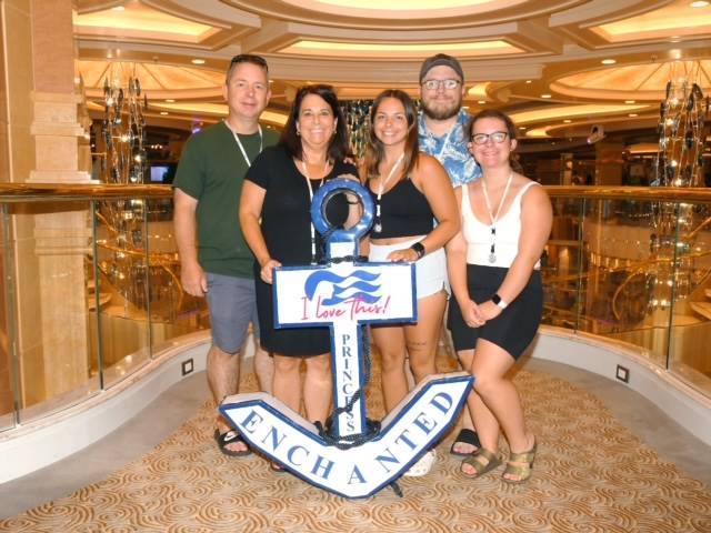 teacher and alumni pose by an anchor while on a cruise