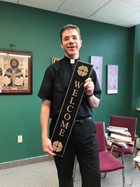 Pastor of St. Brendan holds a welcome sign